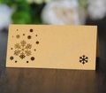 Detalle de tarjeta de mesa dorada con copo de nieve cortado por láser sobre madera - Dorado