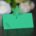 Macro detail of laser-cut green maple leaf place card on a wooden table for weddings - Dark Green