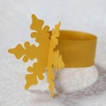 Close-up of laser-cut yellow paper snowflake napkin ring with festive holiday textures - Gold
