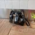 Detail shot of black glossy bucket bag with silver chain and sleek leather strap on wood - Black