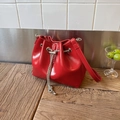 Detail of red leather bucket bag with silver chain and drawstring closure on wooden table - Red