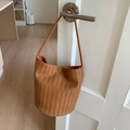 Détail d'un sac seau tressé marron avec motif en V accroché à une poignée de porte - Marron