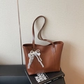 Brown leather tote bag with gold lettering and pearl lace bow charm on art books - Brown