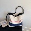 Close-up of canvas bucket bag featuring red and blue stripes with wooden toggle closure - Off White