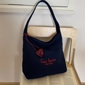 Dettaglio della borsa tote in tela blu navy con ricamo rosso e ciondolo in pelle su sedia - Blu navy