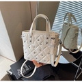 Close-up of cream quilted bucket bag with silver studs and mirror reflection - Off-white