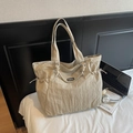 Large beige nylon tote bag with pleated texture and black Fashion label on a bed - Khaki