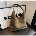 Detalle de bolso hobo de ante verde oliva con correas de cuero marrón sobre madera - Verde