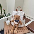 Cream vintage backpack with brown bear pattern and plush bear charm on wooden table - Beige With Charm