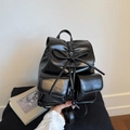 Detail of glossy black leather backpack featuring bow decor and functional front pockets - Black