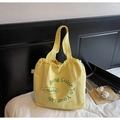 Dettaglio della borsa tote in tela gialla con coulisse e scritte verdi su un letto bianco - Taglia unica / Giallo