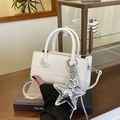 White glossy patent leather crossbody bag with silver star charm in cafe setting - White with Pendant