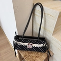 Black polka dot shoulder bag with cream lace trim and red bow detail on a stool - Black