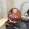 Brown leather shoulder bag with silver studs and a bow, shown in a stylish interior - Brown