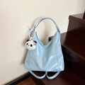 Light blue patent leather tote bag with panda pendant shown on wooden stairs - Blue