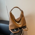 Brown faux leather hobo bag with layered gold chains and pearls on a leather sofa - Brown
