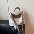 Off-white canvas tote bag with brown leather handles and wide shoulder strap on a sofa - Gray