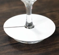 Detail of white round paper wine glass markers on a stemware base for event seating - White