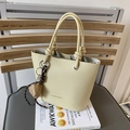 Minimalist beige bucket bag with knotted handle and brown heart charm on a grey chair - With Pendant / Yellow