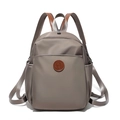 Close-up of taupe nylon backpack featuring brown leather handle and circular logo patch - Gray