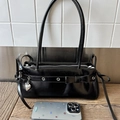 Detalle de bolso negro brillante con lazo, ojales metálicos y colgante de corazón - Negro
