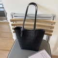 Close-up of black perforated tote bag with scalloped edges on a modern chair - Black