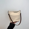 Elegante borsa a secchiello intrecciata beige con tracolla marrone in mano - Albicocca