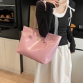 Bolso tote de charol rosa con logotipo dorado llevado por una modelo en un ambiente casual - Rosa