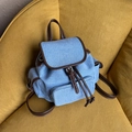 Light blue denim backpack with brown leather trim on a vibrant yellow sofa - Blue