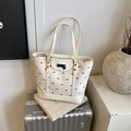 White floral tote bag with red bow embroidery and black heart pendant on metal suitcase - White