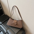 Braune geflochtene Schultertasche mit dekorativer Schleife auf einem Buch - Braun
