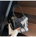 Detail der schwarzen Bucket Bag mit weißer Spitzenschleife und Perlenanhänger auf Buch - Schwarz