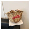 Detail of woven straw beach bag featuring pink Hello embroidery and leather drawstring closure - Red