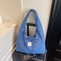 Blue plaid canvas hobo tote bag with drawstring bow and magazine label on a suitcase - Blue