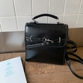 Close-up of black vintage faux leather bag with glossy finish and metal buckle detailing - Black
