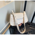 Détail du sac à bandoulière crème avec motif tissé devant une valise noire - Blanc Cassé