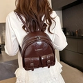 Glossy dark brown mini backpack with twin pockets shown on model in a stylish indoor setting - Brown