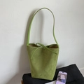 Minimalist green suede bucket bag with bow detail against a white textured wall - Green