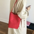 Minimalist red suede bucket bag shown on model wearing a beige trench coat - Red