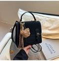 Detail einer schwarzen Handtasche mit goldener Schnalle, Bär-Anhänger und Quaste - Schwarz