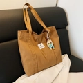 Bolso tote de lona marrón con etiqueta blanca y colgante en un sofá de cuero - Estilo Con Colgante / Marrón con colgante