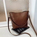 Bolso cubo trenzado marrón oscuro con herrajes plateados sobre libro y mesa blanca - Marrón