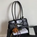 Glossy black baguette shoulder bag with decorative buckle straps and plush puppy pendant - Black (With Charm)