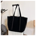 Close-up of black suede tote bag with silver rivets hanging on a white suitcase - Black