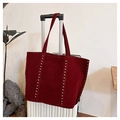 Close-up of burgundy suede tote bag with silver studs hanging on a white suitcase - Burgundy