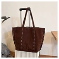 Detailed view of a brown suede tote bag with silver studs hanging on a white suitcase - Coffee