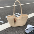Minimalist beige woven tote bag with wooden bead charm on outdoor asphalt surface - Off-white