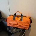 Sac de voyage orange en nylon avec design plissé et bandoulières réglables sur un banc - Orange
