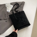 Minimalist black suede tote bag with slim shoulder straps placed on a grey blazer - Black without Pendant
