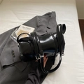 Borsa a tracolla cilindrica nera lucida con doppi cinturini in un ambiente minimalista - Nero